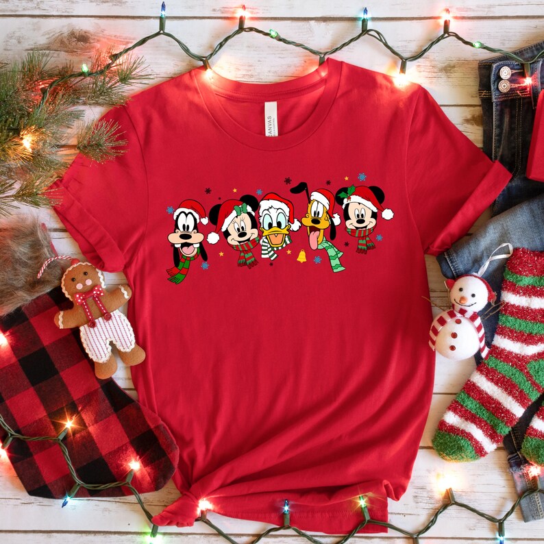 May include: Red t-shirt with a Christmas-themed design featuring Mickey Mouse, Minnie Mouse, Donald Duck, Goofy, and Pluto wearing Santa hats and scarves.