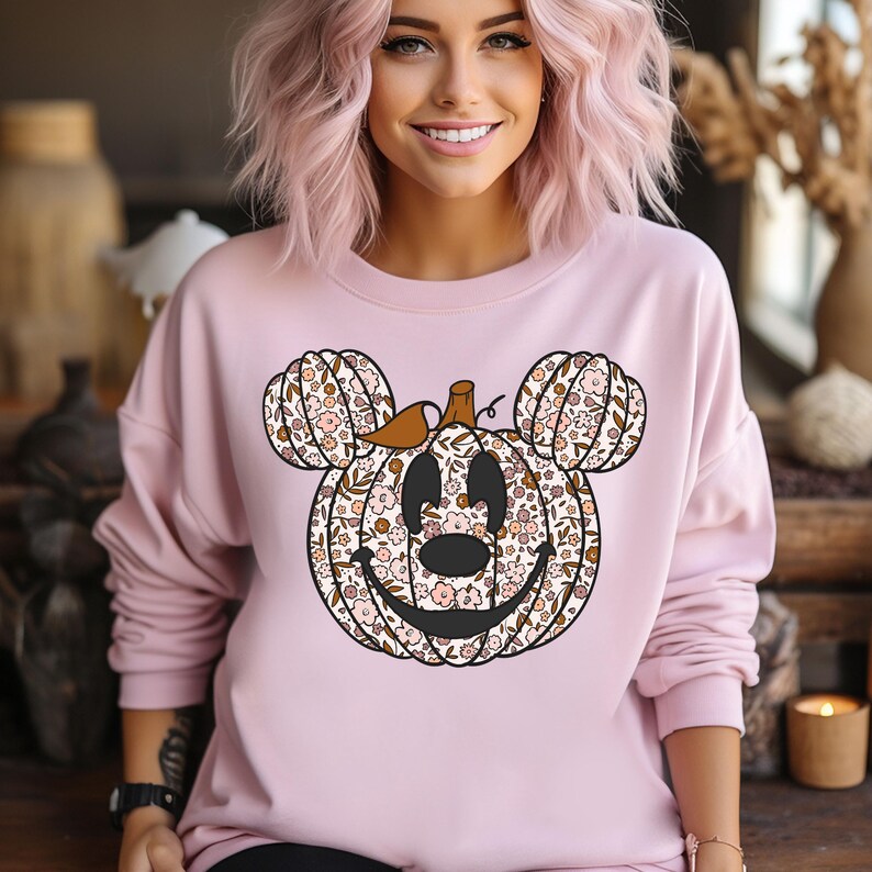 May include: A pink sweatshirt with a floral pumpkin design. The pumpkin is shaped like Mickey Mouse's head.