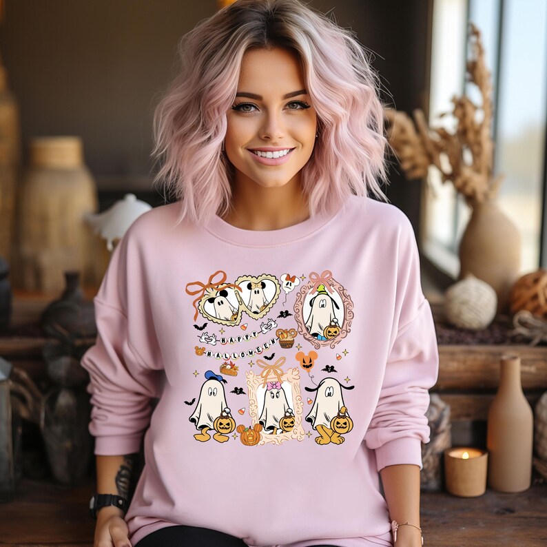 Puede incluir: Sudadera rosa claro con un dise&ntilde;o de Halloween. El dise&ntilde;o presenta fantasmas de dibujos animados sosteniendo calabazas, enmarcados por elementos decorativos. La palabra "HALLOWEEN" tambi&eacute;n est&aacute; impresa en la sudadera.