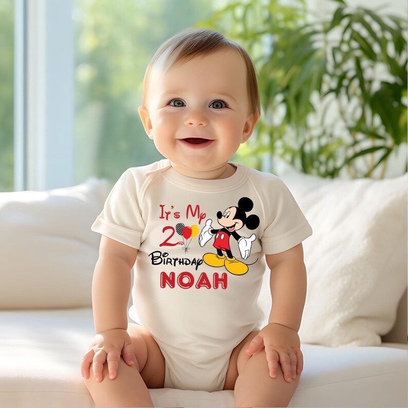 May include: A white bodysuit with a red and black Mickey Mouse graphic. The text "It's My 2nd Birthday NOAH" is printed on the bodysuit.