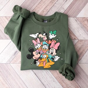 May include: A green sweatshirt with a graphic print of Mickey Mouse, Minnie Mouse, Donald Duck, Goofy, and Pluto. The characters are arranged in a cluster, with Mickey Mouse and Minnie Mouse in the front.