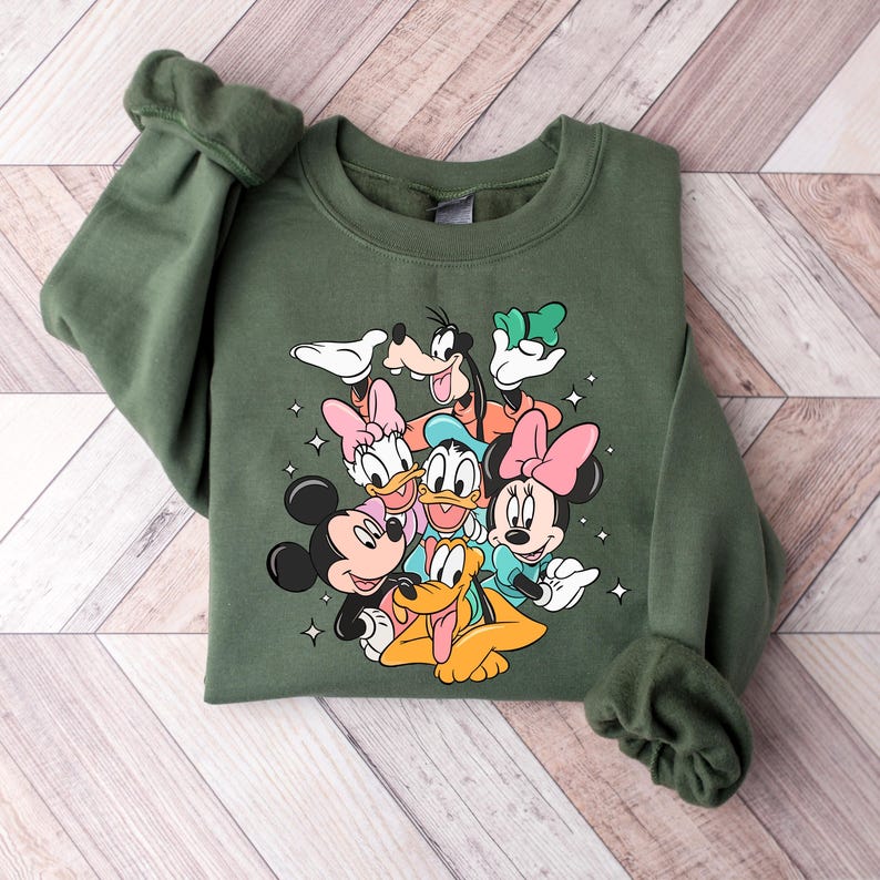 May include: A green sweatshirt with a graphic print of Mickey Mouse, Minnie Mouse, Donald Duck, Goofy, and Pluto. The characters are arranged in a cluster, with Mickey Mouse and Minnie Mouse in the front.