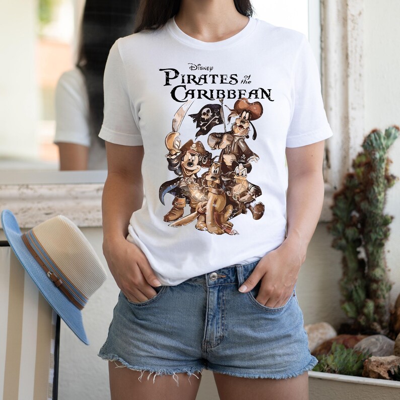 Pode incluir: Camiseta branca com uma estampa gr&aacute;fica de Piratas do Caribe da Disney com Mickey Mouse, Pateta e Pluto vestidos de piratas.