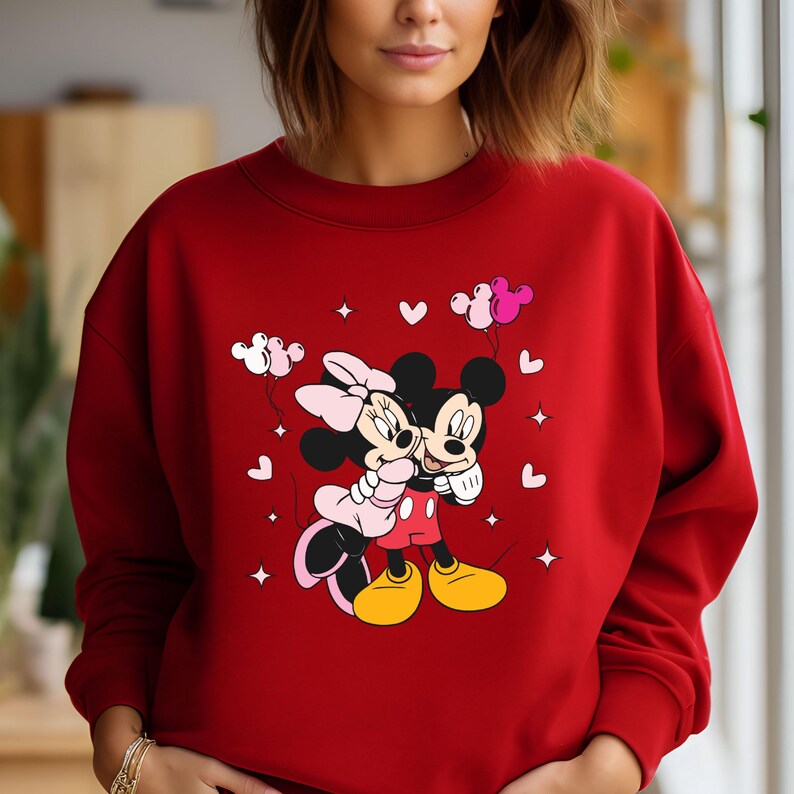 May include: Red sweatshirt with a graphic of Mickey Mouse and Minnie Mouse holding hands with pink balloons and hearts.