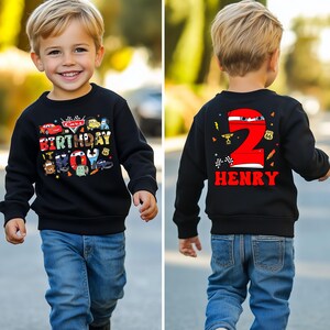 May include: Black sweatshirt with a Cars themed birthday design on the front and a red number 2 with the name Henry on the back. The sweatshirt is being worn by a young child.