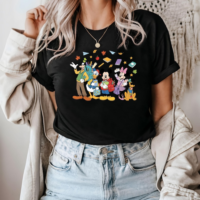 May include: Black t-shirt featuring a colorful graphic of Disney characters, including Goofy, Donald Duck, Mickey Mouse, Minnie Mouse, and Pluto, with books and autumn leaves. The characters are depicted with backpacks, suggesting a back-to-school theme.