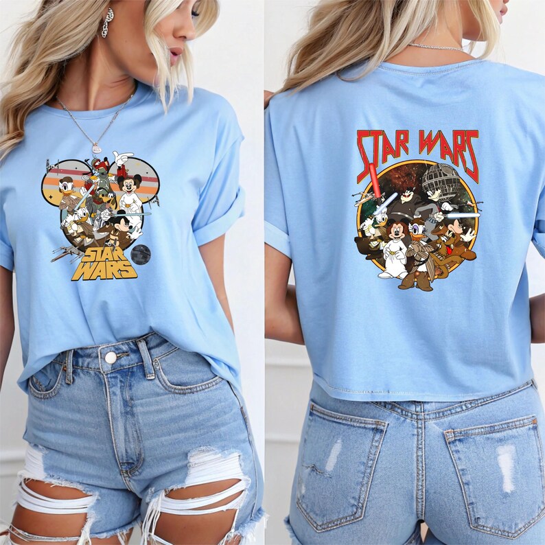 May include: Light blue t-shirt featuring a graphic of Disney characters in a Star Wars theme. The front design is within a Mickey Mouse head shape, and the back has a circular design with the Star Wars logo.