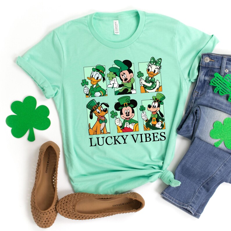 May include: A light green t-shirt with a graphic of Mickey Mouse, Minnie Mouse, Donald Duck, Goofy, and Pluto dressed in green and wearing shamrocks. The text "Lucky Vibes" is printed below the graphic.