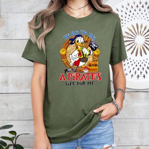 K&ouml;nnte beinhalten: Ein gr&uuml;nes T-Shirt mit einem Cartoon-Bild von Donald Duck, der als Pirat verkleidet ist. Der Text auf dem Shirt lautet "Yo ho yo ho a pirate's life for me".