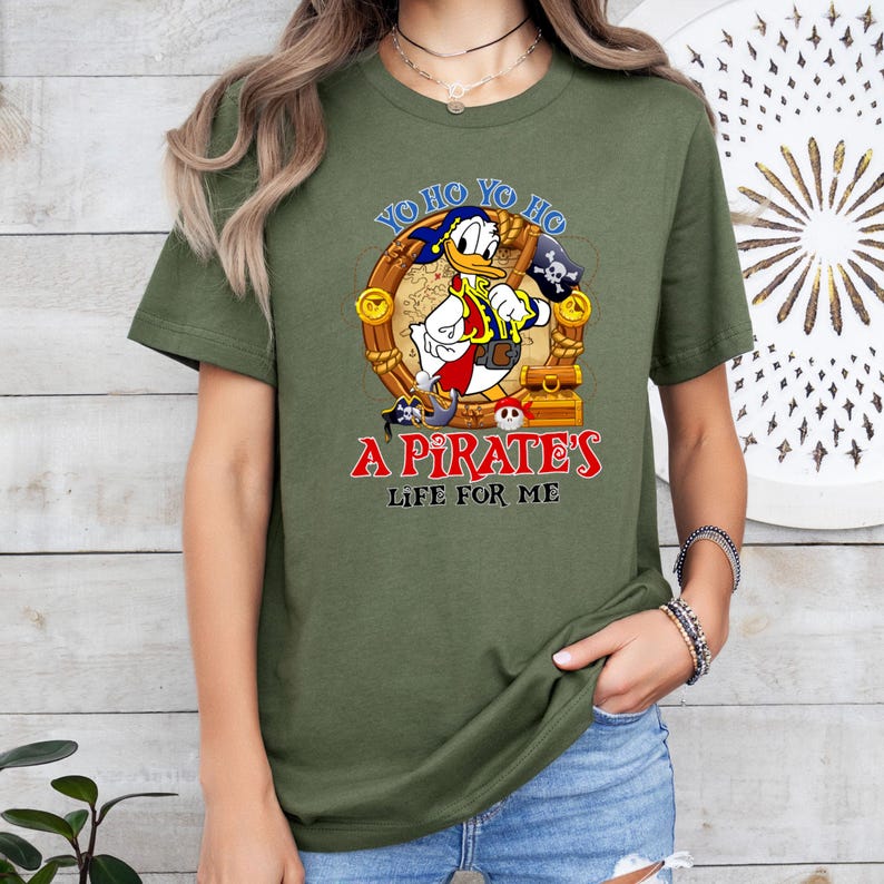 K&ouml;nnte beinhalten: Ein gr&uuml;nes T-Shirt mit einem Cartoon-Bild von Donald Duck, der als Pirat verkleidet ist. Der Text auf dem Shirt lautet "Yo ho yo ho a pirate's life for me".