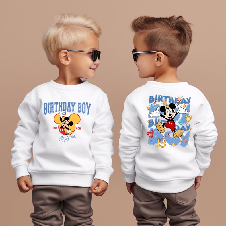 May include: Two white sweatshirts featuring a Mickey Mouse design. One sweatshirt reads "Birthday Boy" with Mickey Mouse's head and "Est. 2013" and "Mickey Mouse" written below. The other sweatshirt has Mickey Mouse in a blue circle with the words "Birthday Boy" around him and the number "13" below him.