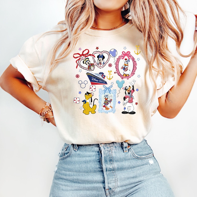 Puede incluir: Una camiseta blanca con un estampado gr&aacute;fico colorido que presenta a Mickey Mouse, Minnie Mouse, Donald Duck y Goofy. El gr&aacute;fico incluye corazones, estrellas, anclas y un crucero. El texto "Disney Cruise Line" es visible en el barco.