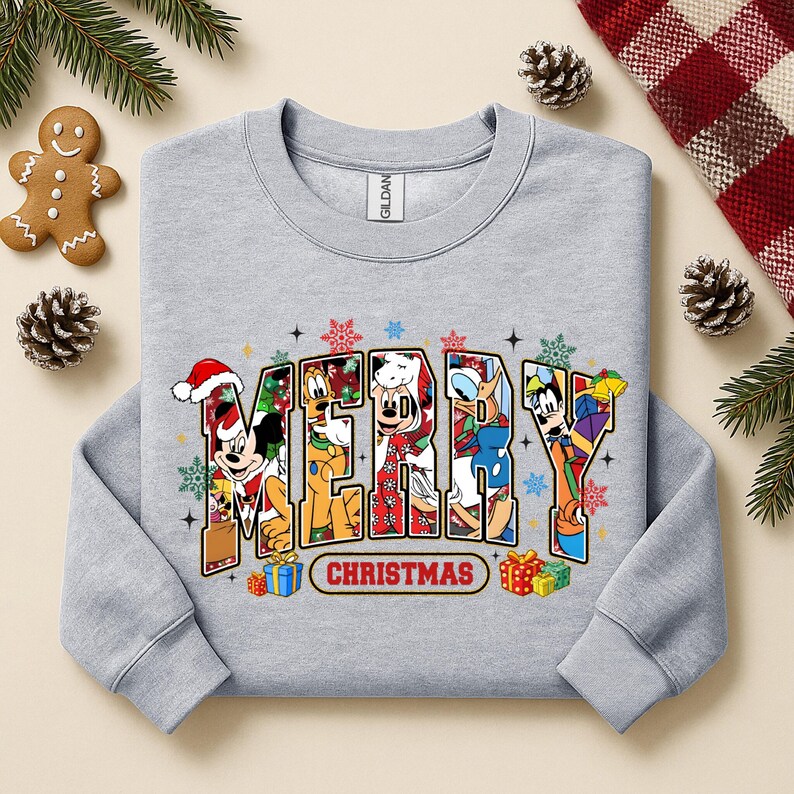 May include: A light gray sweatshirt with the word "MERRY" in colorful letters, each filled with a different Disney character in holiday attire. The word "CHRISTMAS" is below. Festive snowflakes and gift boxes surround the text.