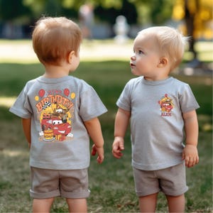 Puede incluir: Dos ni&ntilde;os peque&ntilde;os con camisetas grises con tem&aacute;tica de Cars. Una camiseta dice "It's My Birthday" con un coche de carreras rojo y la otra dice "Alex" con un coche de carreras rojo. Ambas camisetas tienen un fondo gris.