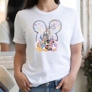 May include: White t-shirt with a watercolor illustration of Mickey Mouse, Minnie Mouse, Donald Duck, Goofy, Pluto, and the Disney castle. The illustration is surrounded by a black outline of Mickey Mouse's ears and fireworks.