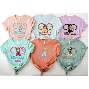 May include: Six different t-shirts featuring Disney princesses with the text "Be Birthday Girl" on each shirt. The princesses featured are Elsa, Belle, Tiana, Anna, Cinderella, and Tiana.