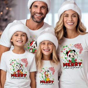 May include: A family of four wearing white t-shirts with a Christmas theme. The shirts feature Mickey Mouse and Pluto with the text "Merry Christmas".