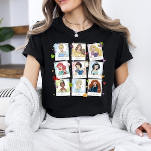 May include: Black t-shirt featuring nine Disney princesses in a grid of polaroid-style frames. Each frame includes a princess illustration and her name. The princesses include Cinderella, Belle, Rapunzel, Ariel, Snow White, Jasmine, Tiana, Elsa, and Merida.