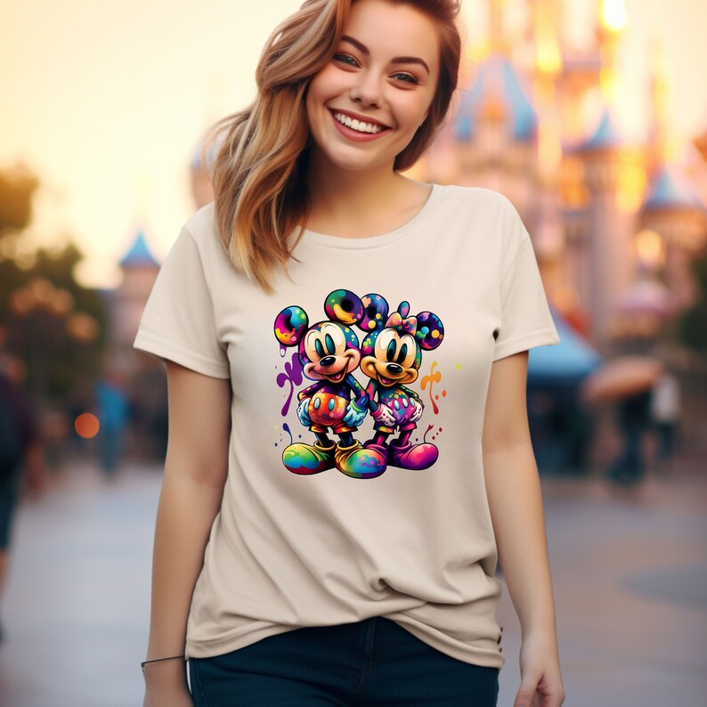 May include: A white t-shirt with a colorful graphic of Mickey Mouse and Minnie Mouse holding hands. The graphic is surrounded by colorful paint splatters.