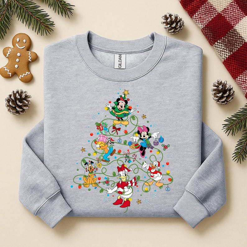 K&ouml;nnte beinhalten: Ein hellgraues Sweatshirt mit einem Weihnachtsbaum-Design aus Disney-Figuren. Micky Maus, Minnie Maus, Donald Duck und Goofy sind mit farbenfrohen Weihnachtsdekorationen dargestellt. Das Sweatshirt hat einen Rundhalsausschnitt und lange &Auml;rmel.