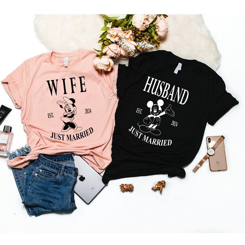 May include: Two t-shirts, one pink and one black, with the words "Wife" and "Husband" printed on them. Each shirt features a cartoon image of Mickey Mouse or Minnie Mouse and the text "Est. 2024 Just Married".