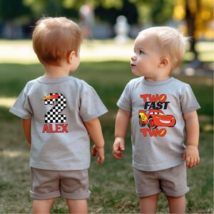 K&ouml;nnte beinhalten: Zwei junge Kinder tragen passende graue T-Shirts und Shorts. Ein Shirt zeigt eine karierte Nummer 2 mit dem Namen "ALEX" in Rot. Das andere Shirt hat eine rote Rennwagen-Grafik mit den Worten "TWO FAST TWO".
