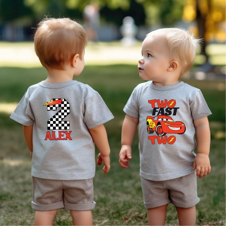 K&ouml;nnte beinhalten: Zwei junge Kinder tragen passende graue T-Shirts und Shorts. Ein Shirt zeigt eine karierte Nummer 2 mit dem Namen "ALEX" in Rot. Das andere Shirt hat eine rote Rennwagen-Grafik mit den Worten "TWO FAST TWO".