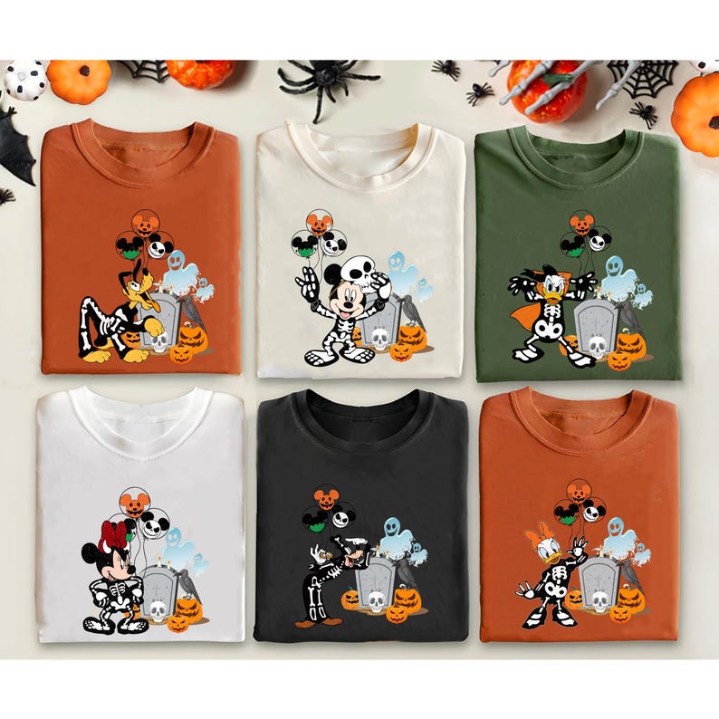 May include: Six Halloween-themed t-shirts in various colors, each featuring a cartoon character in a skeleton costume. The designs include Mickey Mouse, Minnie Mouse, Donald Duck, and Pluto, with pumpkins and tombstones. The shirts are orange, cream, green, white, black, and rust.