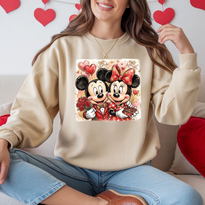 May include: Beige sweatshirt featuring a colorful graphic of Mickey and Minnie Mouse in formal attire, holding roses and chocolates. The design includes heart-shaped balloons and a Valentine's Day theme.