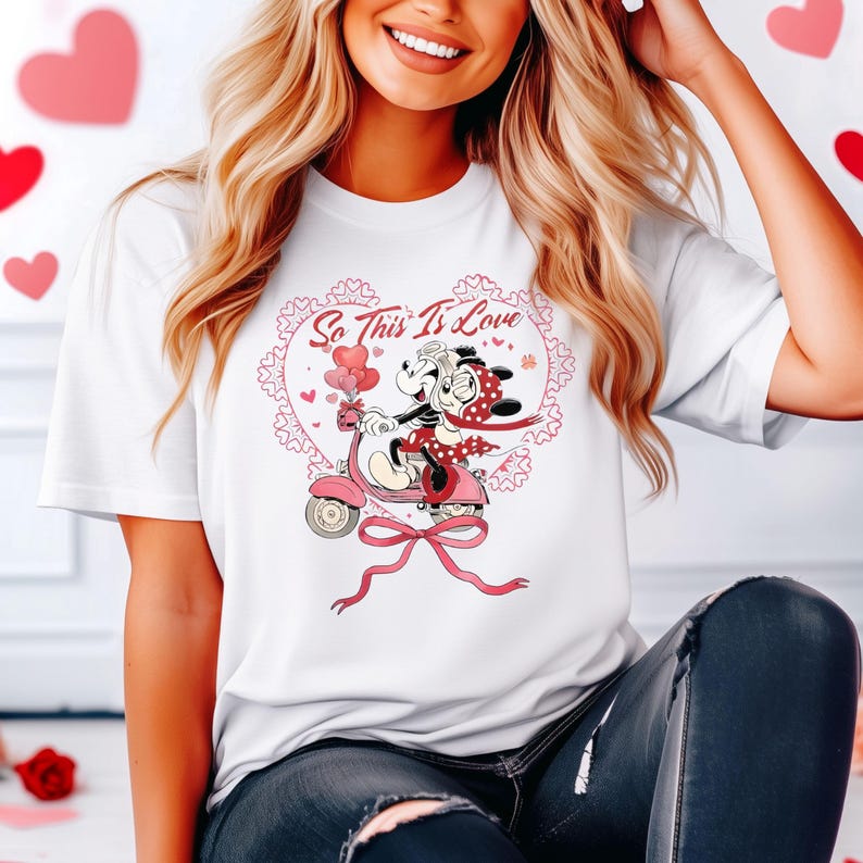 Puede incluir: Camiseta blanca con una ilustraci&oacute;n de dibujos animados de dos ratones en un scooter rosa, con el texto "So This Is Love" dentro de un dise&ntilde;o en forma de coraz&oacute;n. El dise&ntilde;o incluye corazones rojos y una cinta rosa. Una camiseta gr&aacute;fica con tem&aacute;tica de San Valent&iacute;n.