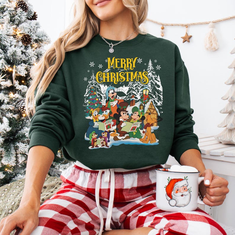 May include: Green Christmas sweatshirt with a festive scene of Mickey Mouse and friends singing carols. The text "Merry Christmas" is printed in yellow on the front of the sweatshirt.