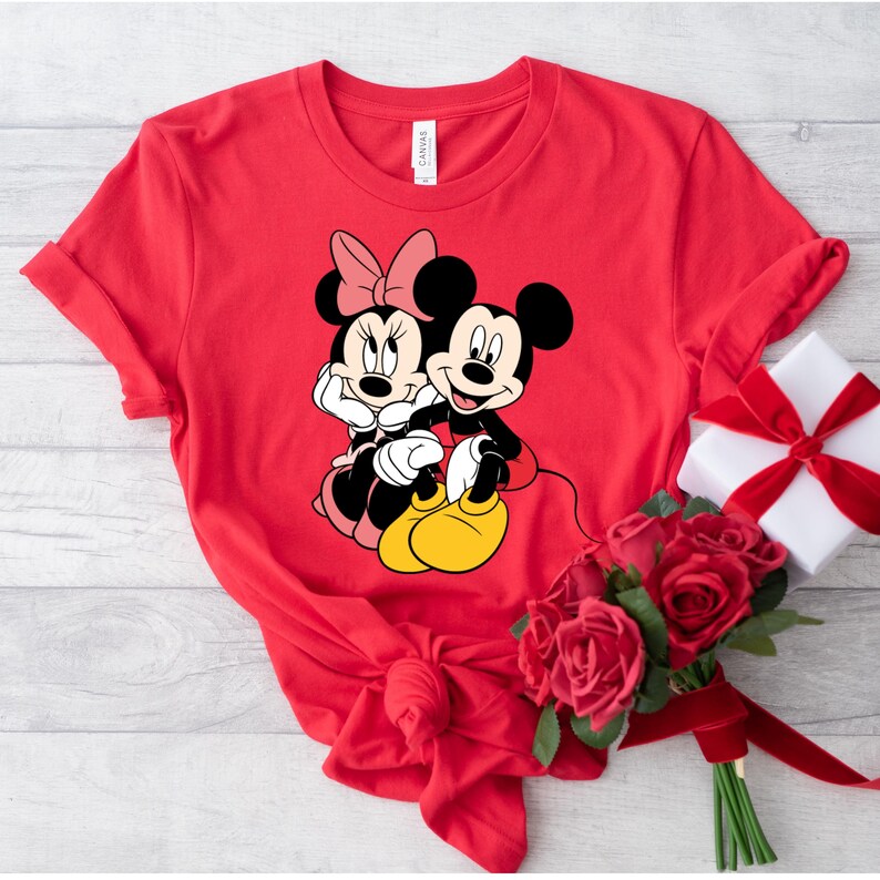 May include: Red t-shirt with a graphic of Mickey Mouse and Minnie Mouse holding hands.