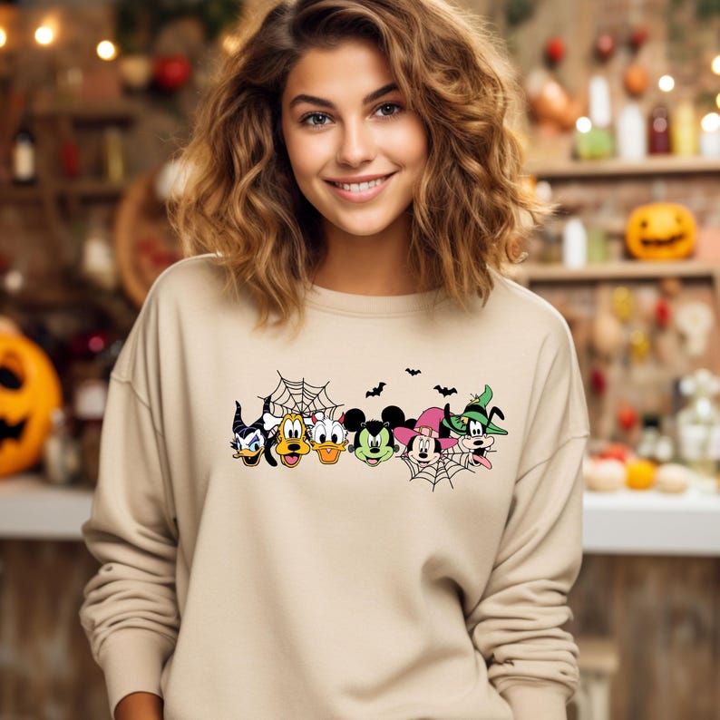 Pu&ograve; includere: Una felpa beige con un design a tema Halloween con Topolino, Minnie Mouse, Paperino, Pippo e Pluto. I personaggi sono vestiti in costume e circondati da ragnatele e pipistrelli.