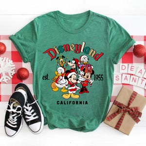 May include: Green t-shirt with a vintage Disneyland logo featuring Mickey Mouse and friends in Christmas attire. The text reads "Disneyland est. 1955 California".