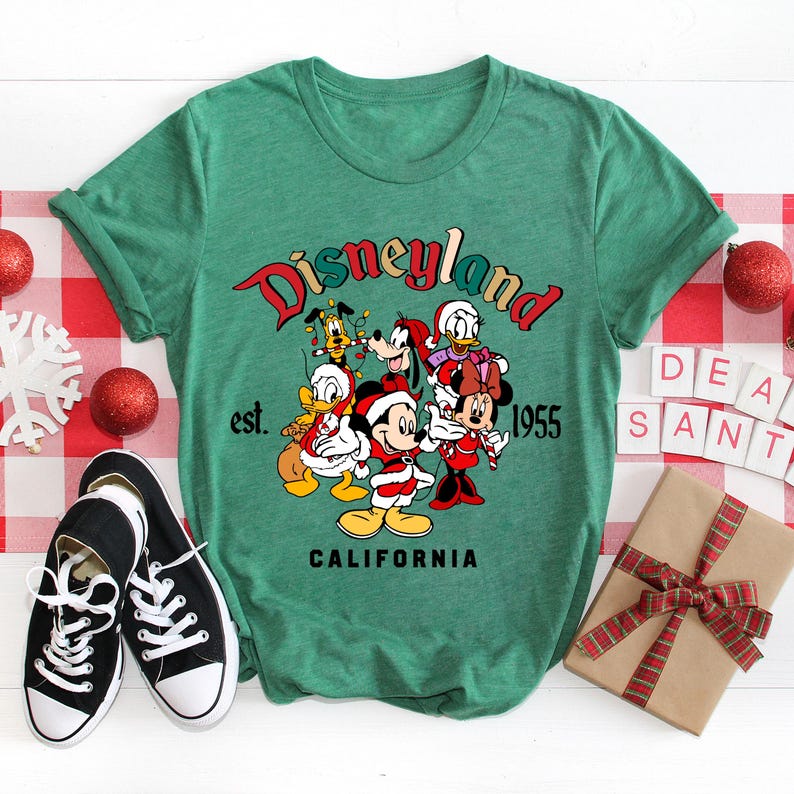 May include: Green t-shirt with a vintage Disneyland logo featuring Mickey Mouse and friends in Christmas attire. The text reads "Disneyland est. 1955 California".
