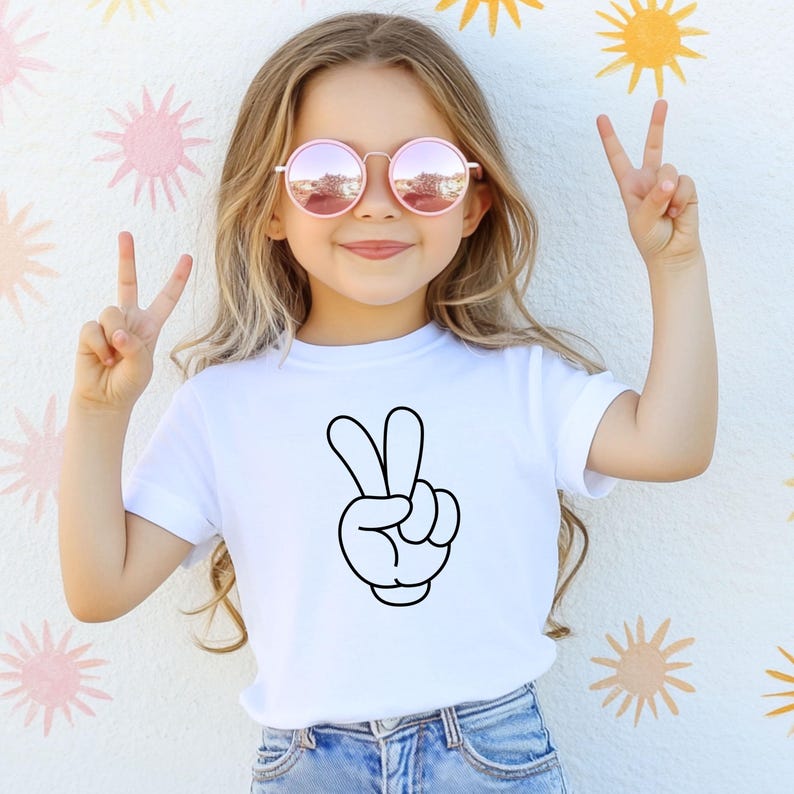 K&ouml;nnte beinhalten: Ein wei&szlig;es T-Shirt mit einem schwarzen Cartoon-Friedenszeichen. Die Person auf dem Bild tr&auml;gt rosa get&ouml;nte runde Sonnenbrillen und macht mit ihren Fingern ein Friedenszeichen. Der Hintergrund ist eine wei&szlig;e Wand mit gelben und rosa sonnenf&ouml;rmigen Designs.