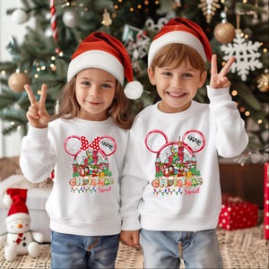 Puede incluir: Dos ni&ntilde;os con sudaderas navide&ntilde;as blancas con un dise&ntilde;o tem&aacute;tico de Mickey Mouse. Las sudaderas tienen el texto "Christmas Squad" y un nombre personalizable. Ambos ni&ntilde;os llevan gorros de Pap&aacute; Noel rojos.