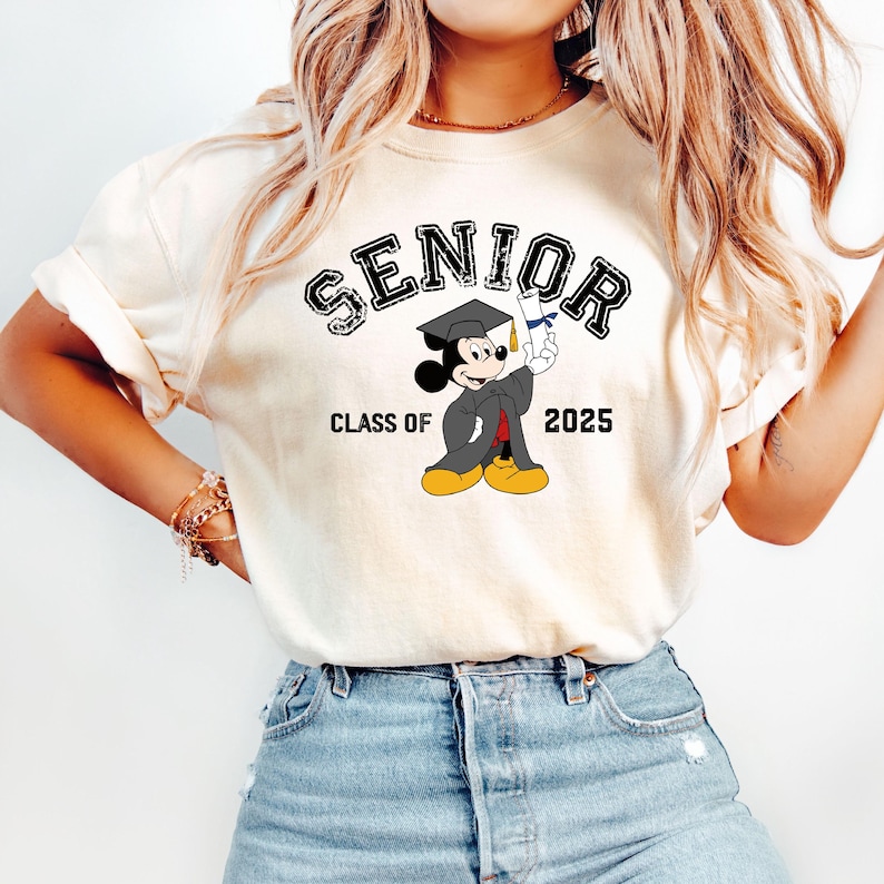 Op de afbeelding: Wit T-shirt met een zwarte afbeelding van Mickey Mouse die een afstudeerpet draagt en een diploma vasthoudt. De tekst "Senior Class of 2025" is onder de afbeelding gedrukt.