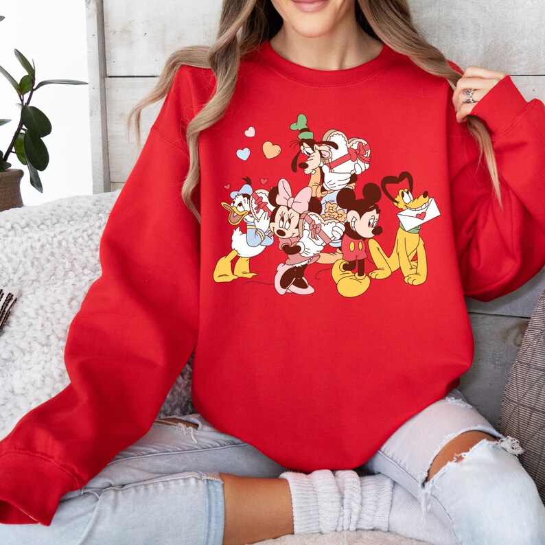 May include: Red sweatshirt with a graphic print of Mickey Mouse, Minnie Mouse, Donald Duck, Goofy, and Pluto. The characters are holding hearts and gifts.