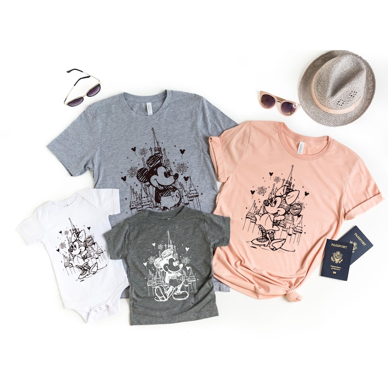 May include: A set of three t-shirts featuring a black and white illustration of Mickey Mouse and Minnie Mouse in front of Cinderella's Castle. The shirts are in grey, peach, and white.