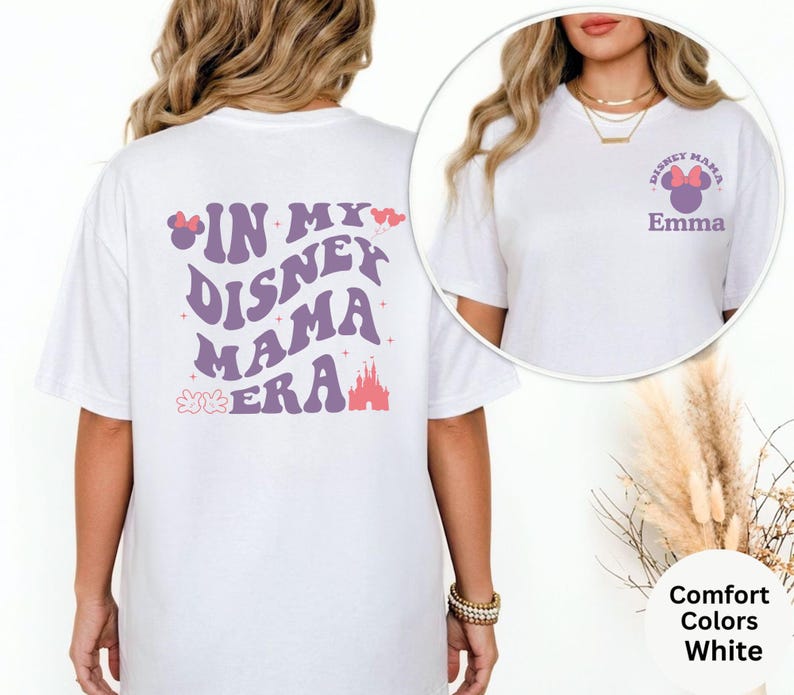 Puede incluir: Camiseta blanca con el texto "IN MY DISNEY MAMA ERA" en morado, rosa y rojo. La parte delantera de la camiseta tiene el texto "DISNEY MAMA" con un lazo de Minnie Mouse y el nombre "Emma". La camiseta es de la marca Comfort Colors.