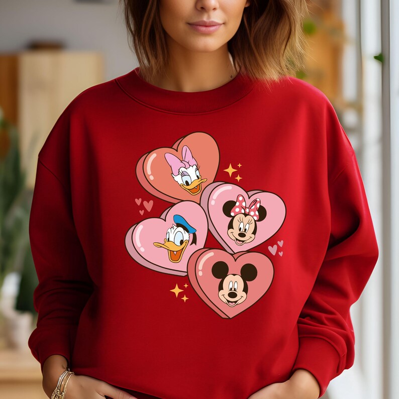 Puede incluir: Sudadera roja con un gr&aacute;fico de Mickey Mouse, Minnie Mouse, Donald Duck y Daisy Duck en cajas de dulces con forma de coraz&oacute;n. Los personajes sonr&iacute;en y tienen sus caracter&iacute;sticas distintivas.