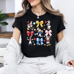 May include: Black t-shirt with a colorful print of Disney characters wearing sailor outfits and bows. The characters include Mickey Mouse, Minnie Mouse, Donald Duck, and Goofy.