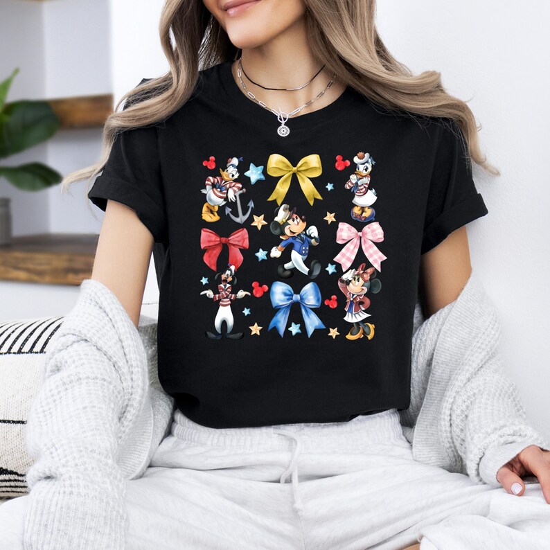 May include: Black t-shirt with a colorful print of Disney characters wearing sailor outfits and bows. The characters include Mickey Mouse, Minnie Mouse, Donald Duck, and Goofy.