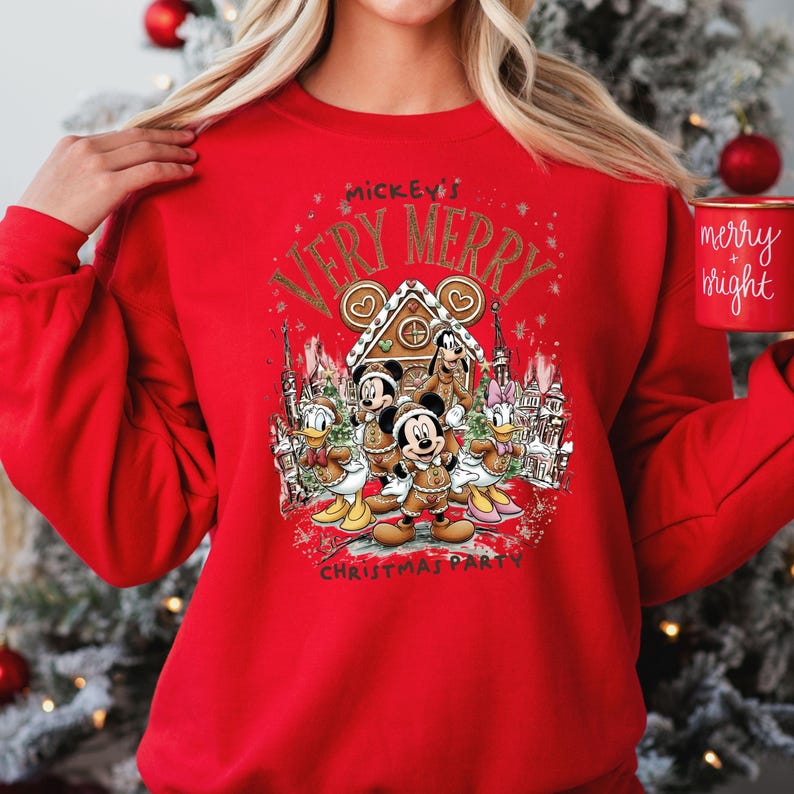 Puede incluir: Una sudadera roja con un dise&ntilde;o festivo que presenta a Mickey Mouse y sus amigos. El dise&ntilde;o incluye el texto "Mickey's Very Merry Christmas Party" y una casa de jengibre. Tambi&eacute;n se ve una taza roja con "merry + bright".