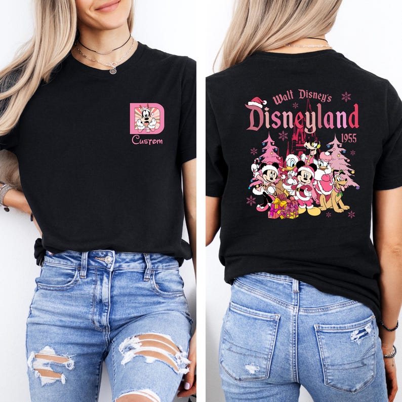 May include: Black t-shirt featuring a pink and white graphic of Mickey Mouse inside a pink letter "D" on the front. The back of the shirt displays a Disneyland 1955 design with Disney characters and Christmas trees.