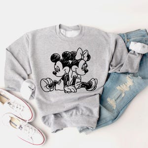 May include: A gray sweatshirt with a black and white illustration of Mickey Mouse and Minnie Mouse holding hands. The illustration is in a cartoon style.