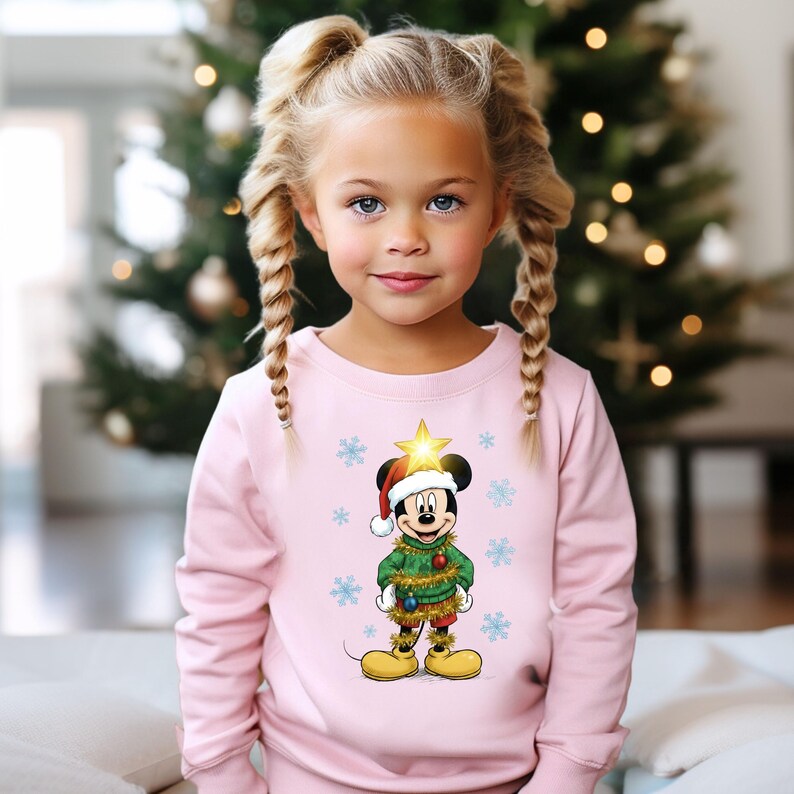Pode incluir: Uma camisola rosa com um design do Mickey Mouse com tema natalino. Mickey est&aacute; usando um gorro de Papai Noel, um su&eacute;ter verde e enfeites dourados. O design inclui flocos de neve e uma estrela na cabe&ccedil;a do Mickey. Uma &aacute;rvore de Natal est&aacute; no fundo.