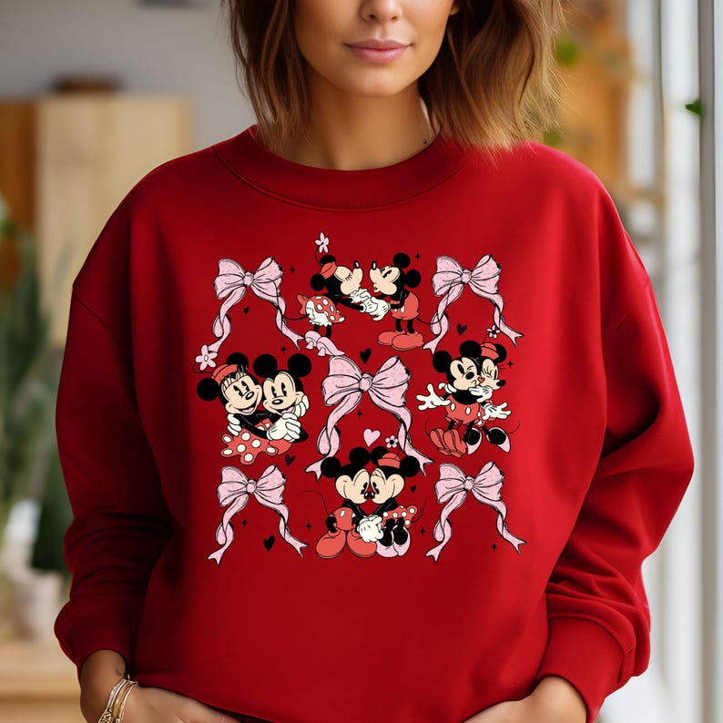 May include: Red sweatshirt with a graphic print of Mickey Mouse and Minnie Mouse in various poses. The print features pink bows and hearts.
