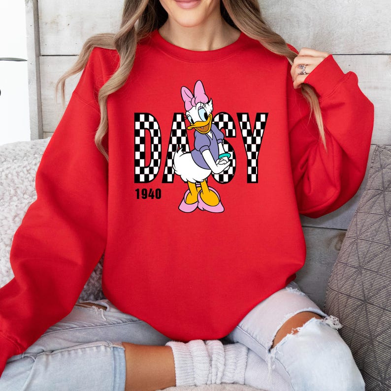 May include: Red sweatshirt with a checkered design and the word "DAISY" in white letters. A cartoon image of Daisy Duck is in the center of the design. The year "1940" is printed below the design.